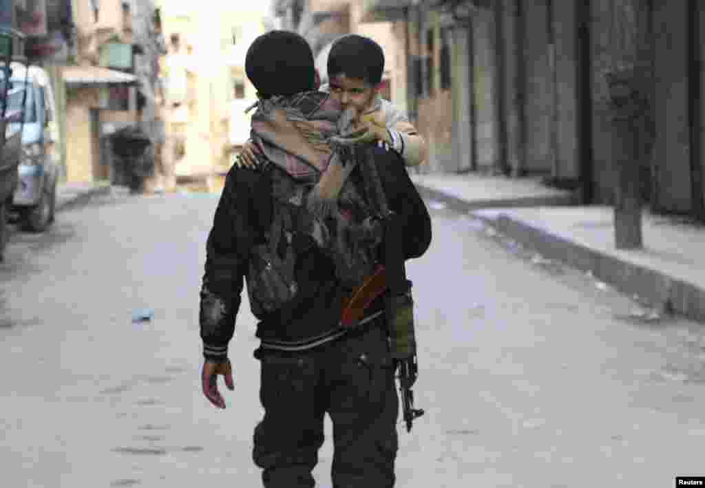 A Kurdish fighter from the Popular Protection Units (YPG) carries his son as he walks along a street, Sheikh Maqsoud neighborhood, Aleppo, Feb. 18, 2014.&nbsp;