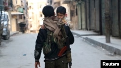 FILE - A Kurdish fighter from the People's Protection Units (YPG) carries his son as he walks along a street in Aleppo's Sheikh Maqsoud neighborhood, Feb. 18, 2014. Rebels with the Army of Islam and their allies said Tuesday they will continue fighting in the predominantly Kurdish neighborhood, despite a cease-fire.