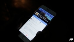 In this March 1, 2016 photo, a man views Cambodian Prime Minister Hun Sen's Facebook page on his mobile phone at a sidewalk in downtown Phnom Penh, Cambodia. Cambodia’s long-ruling Hun Sen and exiled opposition leader Sam Rainsy have gotten an early start