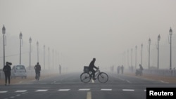 FILE - A newspaper vendor rides his bicycle on a smoggy morning in New Delhi, India, Dec. 1, 2015.