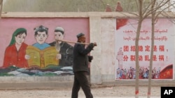 FILE - A farmer walks past government propaganda depicting ethnic minority residents reading the constitution with slogans that read, "Unity and Stability is fortune, Separatism and Turmoil is misfortune," near Kashgar in northwestern China's Xinjiang Uyghur Autonomous Region on March 19, 2021.