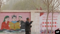 FILE - A farmer walks past propaganda depicting ethnic minority residents reading the constitution with slogans which reads, "Unity Stability is fortune, Separatism and Turmoil is misfortune," near Kashgar in China’s Xinjiang Uyghur Autonomous Region on March 19, 2021.