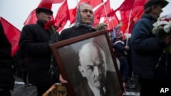 FILE - A woman carries a portrait of Lenin as she walks with the Communist Party members and supporters to place flowers at the Tomb of Soviet founder Vladimir Lenin, at Moscow's Red Square, Nov. 6, 2014.