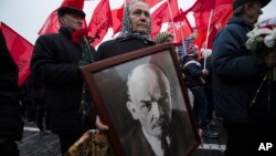 FILE - A woman carries a portrait of Lenin as she walks with the Communist Party members and supporters to place flowers at the Tomb of Soviet founder Vladimir Lenin, at Moscow's Red Square, Nov. 6, 2014. On Monday, Jan. 25, 2016, Russian President Vladimir Putin has criticized the regime of Soviet founder Vladimir Lenin and sharply denounced brutal repressions by the Bolshevik government. 