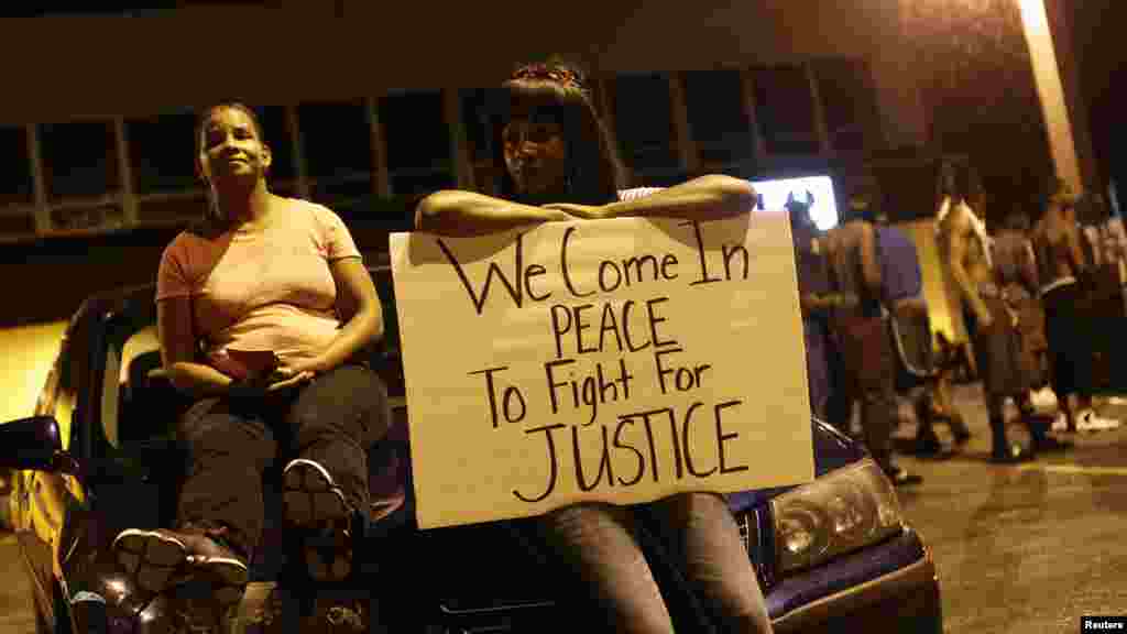 Demonstrators protesting the shooting death of Michael Brown rest on a car while holding a sign in Ferguson, Missouri, Aug. 19, 2014. 