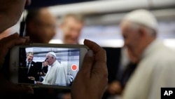 FILE - A journalists uses his mobile phone to take a picture of Pope Francis aboard the papal airplane.