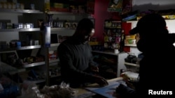 A shopkeeper counts change by the light of a battery-powered lamp during a load-shedding electricity blackout in Cape Town, South Africa Taken 4.15.2015