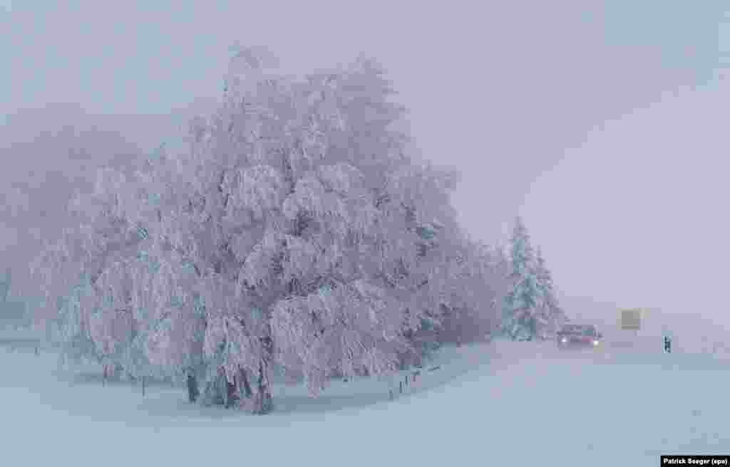 A car passes snow-covered trees near Hofsgrund, Germany.