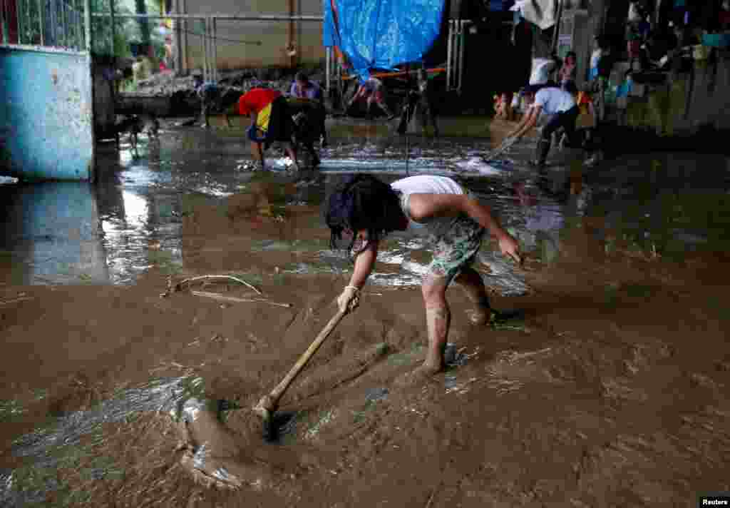 Warga membersihkan lumpur yang dibawa oleh banjir di pusat penampungan pengungsi di San Mateo, Rizal, Filipina.