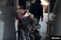 A girl with her father in a wheelchair asks for help from passers-by to pay a medical bill, in Douma, Syria, Feb. 3, 2016.