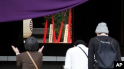 Religious offerings dedicated by Japanese Prime Minister Shinzo Abe are seen, center in the background, as people pray at the Yasukuni Shrine in Tokyo, where a woman claps to offer prayers for those who died during World War II, April 21, 2015. 