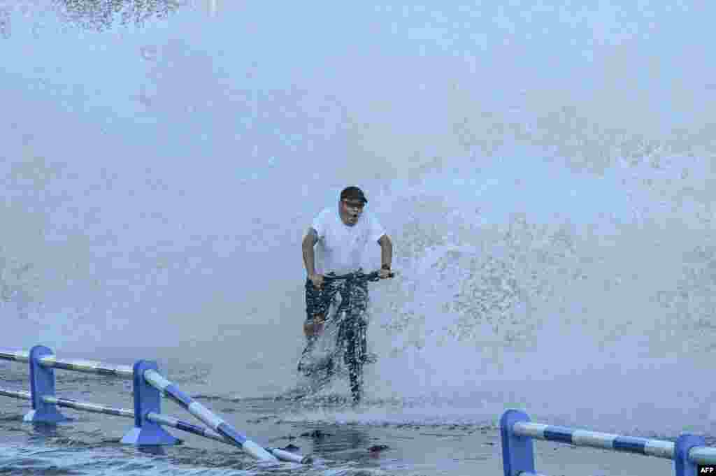 A man rides a bicycle as waves, caused by Typhoon In-Fa further down the Chinese coast, surge over a barrier along the seacoast in Qingdao in China&#39;s eastern Shandong province, July 25, 2021.