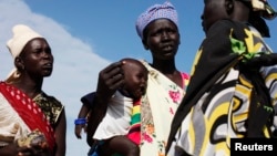A woman carries a baby as she talks with other women talk at a food distribution center in Minkaman, Lakes State, South Sudan, June 27, 2014.