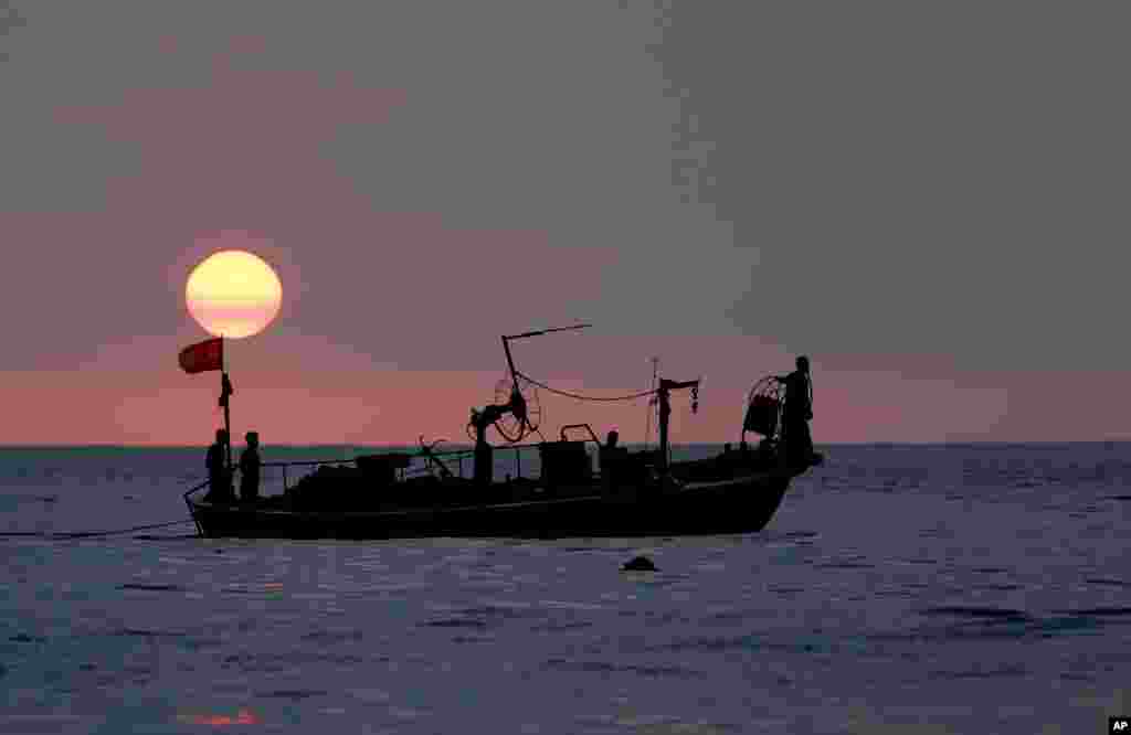 Fishermen sit at the bow of a fishing boat in the Mediterranean Sea as the sun sets, at Ramlet al-Baida public beach, in Beirut, Lebanon.