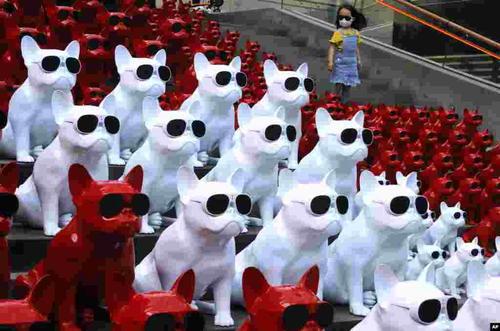 A child wearing a mask walks past audio speakers in the shape of dogs displayed at a shopping area in Beijing, China.