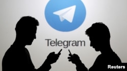 FILE - Two men pose with smartphones in front of a screen showing the Telegram messenger app logo in a picture illustration taken Nov. 18, 2015.