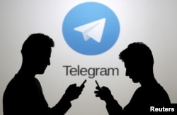 FILE - Two men pose with smartphones in front of a screen showing the Telegram logo in this picture illustration taken in Zenica, Bosnia and Herzegovina, Nov. 18, 2015.