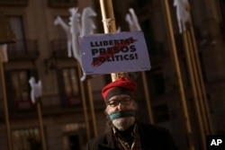 A man stands next to a banner reading in Catalan: "Freedom for Political Prisoners", in support of Catalonia politicians who have been jailed on charges of sedition in Barcelona, Spain, Dec. 19, 2017.