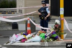 Police stand by a collection of flowers near the Linwood mosque in Christchurch, New Zealand, March 16, 2019, where one of the two mass shootings occurred.