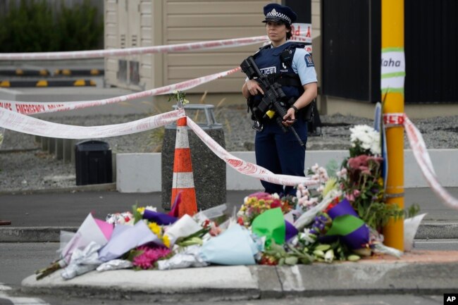 Police stand by a collection of flowers near the Linwood mosque in Christchurch, New Zealand, March 16, 2019, where one of the two mass shootings occurred.
