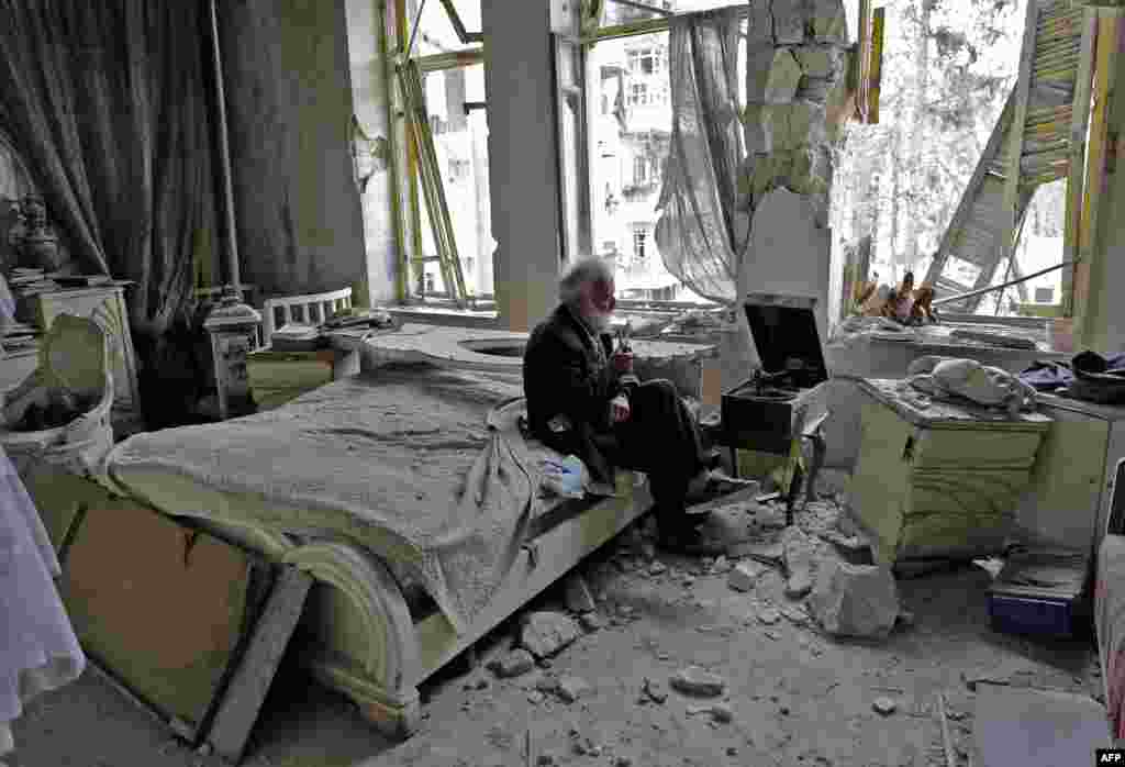 Mohammed Mohiedin Anis, or Abu Omar, 70, smokes his pipe as he sits in his destroyed bedroom listening to music on his vinyl player, gramophone, in Aleppo's formerly rebel-held al-Shaar neighborhood.
