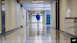 FILE - A middle school principal walks the empty halls of his school as he speaks with one of his teachers about her COVID-19 symptoms, in Wrightsville, Ga., Aug., 20, 2021. On Dec. 27, 2021, U.S. health officials cut isolation restrictions for Americans 
