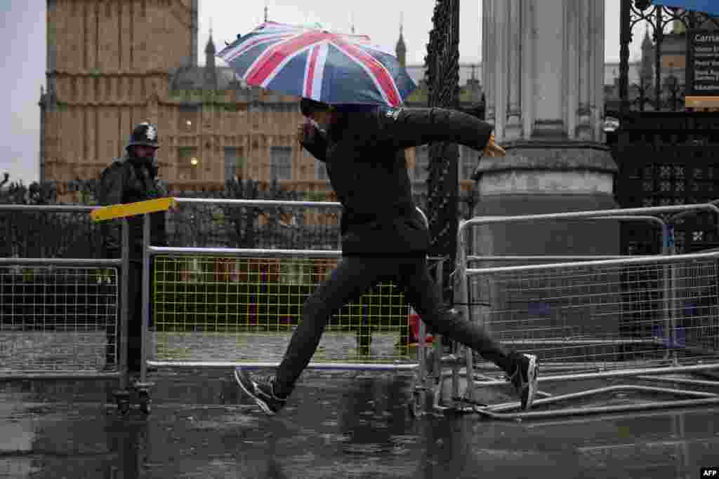 Seorang pejalan kaki melompati genangan air di trotoar di luar Gedung Parlemen, London tengah.