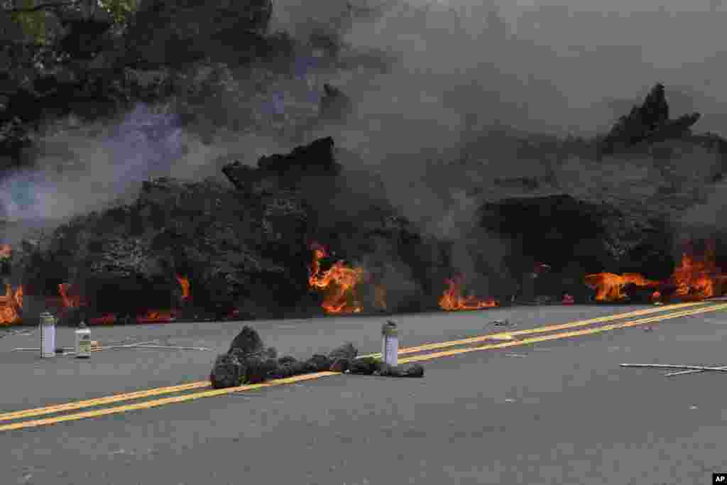 In this Saturday, May 5, 2018, photo, lava burns across a road as an offering to the volcano goddess lies in the foreground in the Leilani Estates subdivision near Pahoa, Hawaii. Glowing plumes of lava have shot many meters into the air at points, officia