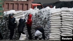 FILE - North Koreans distribute imported sacks of flour on the banks of Yalu River, near the North Korean town of Sinuiju, opposite the Chinese border city of Dandong.