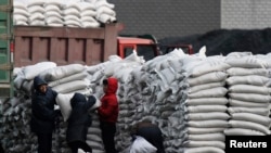 FILE - North Koreans distribute imported sacks of flour on the banks of Yalu River, near the North Korean town of Sinuiju, opposite the Chinese border city of Dandong, Jan. 27, 2014. 