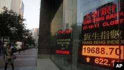 A woman walks past a screen displaying the Hang Seng stock index in Hong Kong, October 27, 2011.