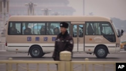 FILE - A vehicle carries the delegates passing by Tiananmen Square as a police officer stands guard next to main road.