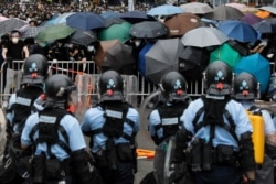 Policemen in anti-riot gear stand watch as protesters use umbrellas to shield themselves near the Legislative Council in Hong Kong, Wednesday, June 12, 2019.