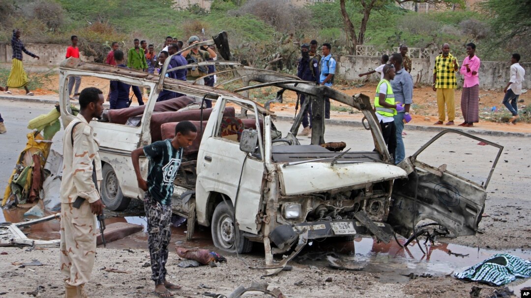 Seorang tentara Somalia (kiri) berdiri di dekat reruntuhan minibus yang hancur akibat serangan bom dekat kompleks Kementerian Pertahanan di Mogadishu, Somalia, 9 April 2017. (AP Photo/Farah Abdi Warsameh)