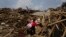 A woman carries her salvaged goods through the rubble of destroyed houses following a massive earthquake in the town of Longtoushan in Ludian County in southwest China's Yunnan Province Wednesday, Aug. 6, 2014.