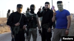 FILE - Rebels from the Hayat Tahrir al-Sham group are seen near buses, outside the villages of al-Foua and Kefraya, Idlib province, Syria, July 18, 2018. 