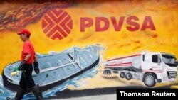 Foto de archivo de un trabajador que pasa frente a un mural con el logo de PDVSA en una gasolinera de Caracas.