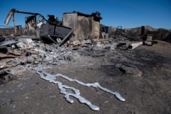 Debris from a hilltop home smolders after being burned by the Tick Fire, Oct. 25, 2019, in Santa Clarita, Calif. An estimated 50,000 people were under evacuation orders in the Santa Clarita area north of Los Angeles.