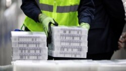 FILE - Pfizer employees handle containers of vaccine doses at a Pfizer manufacturing plant producing the coronavirus vaccine, in Kalamazoo, Michigan, Feb. 19, 2021.