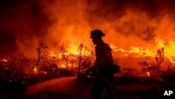 FILE - A firefighter hoses down areas of the Dixie Fire as it jumps Highway 395 south of Janesville, California on August 16, 2021. (AP Photo/Ethan Swope)