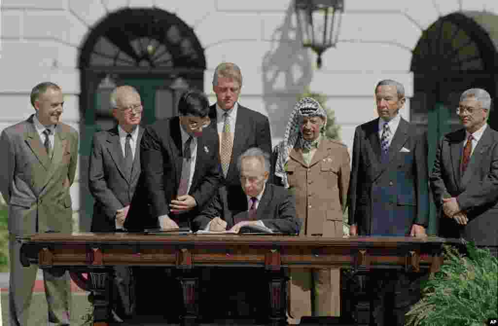 1993 Mideast Peace Agreement: Israeli Foreign Minister Shimon Peres signs the Mideast Peace Agreement on the South Lawn of the White House in Washington, D.C., as President Clinton, standing center, PLO Chairman Yasser Arafat, third from right, and other 