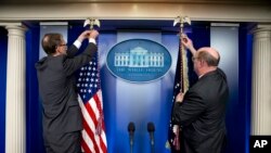 Dos empleados de la Casa Blanca preparan las banderas antes de la llegada del presidente Barack Obama a la sala de crisis sobre Ucrania.