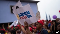 ARCHIVO - Una mujer sostiene un cartel que lee: "Biden, levante el bloqueo ahora" en una manifestación en apoyo al presidente venezolano Nicolás Maduro y contra las sanciones estadounidenses a Venezuela, en el barrio Junquito de Caracas, Venezuela, el martes 18 de junio de 2024.