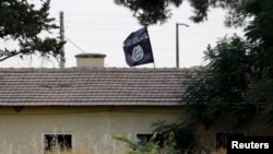 FILE - An Islamic State flag flies over the customs office of Syria's Jarablus border gate as seen from the Turkish town of Karkamis, in Gaziantep province, Turkey, Aug. 1, 2015.