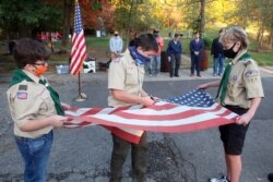 Boy Scouts pack 380 use scissors to cut a worn out American flag before burning it in barrel fires as part of a flag retirement ceremony at a park in Slippery Rock, Pennsylvania, Oct, 13, 2020.