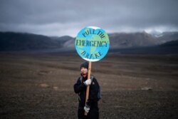 A girl holds a sign that reads 'pull the emergency brake' as she attends a ceremony in the area which once was the Okjokull glacier, in Iceland, Aug. 18, 2019.