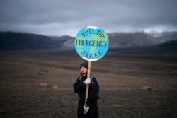 A girl holds a sign that reads 'pull the emergency brake' as she attends a ceremony in the area which once was the Okjokull glacier, in Iceland, Aug. 18, 2019.