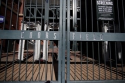 The bars from the closed gate cast long shadows into Coors Field, the home of MLB's Colorado Rockies, as a stay-at-home order takes effect to reduce the spread of the coronavirus, March 26, 2020, in Denver.