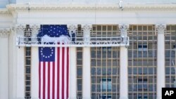 FILE - Workers install a flag on the West Front of the U.S. Capitol as preparations take place for President-elect Joe Biden's inauguration, Jan. 9, 2021.