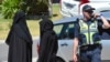 Dua wanita berdiri di dekat seorang polisi yang tengah memblokir jalan saat menggeledah sebuah rumah di pinggiran Melbourne Meadow Heights, Australia, 23 Desember 2016. (AAP/Julian Smith/via REUTERS)